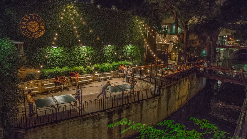 exterior view of Easy Tiger in Austin, TX. Patrons sip beer and play pin-pong under fairy lights on the patio