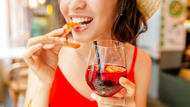 a woman bites into a shrimp and holds a mimosa in a seafood restaurant