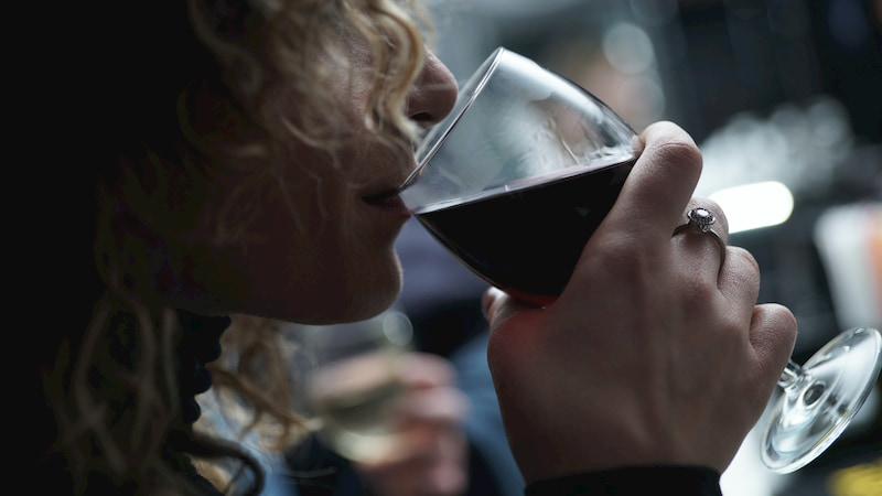 a woman takes a sip of red wine at a darkened restaurant space