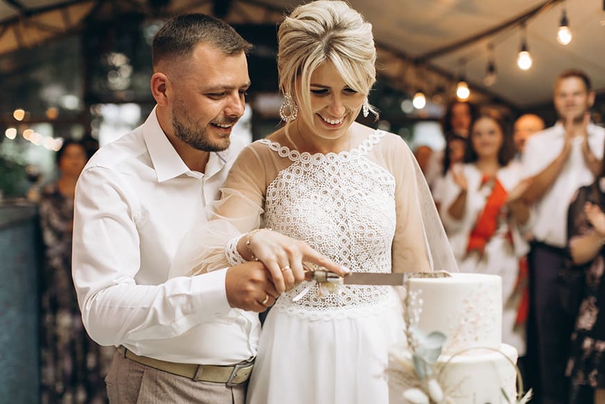 Bride and groom cut their wedding cake with guests behind them